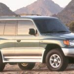 Grüner Mitsubishi Montero von 1998 in Front-Dreiviertelansicht vor Bergen