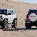 Zwei Ford Bronco Outer Banks 60th Anniversary in Front- und Heckansicht vor einer Sanddüne