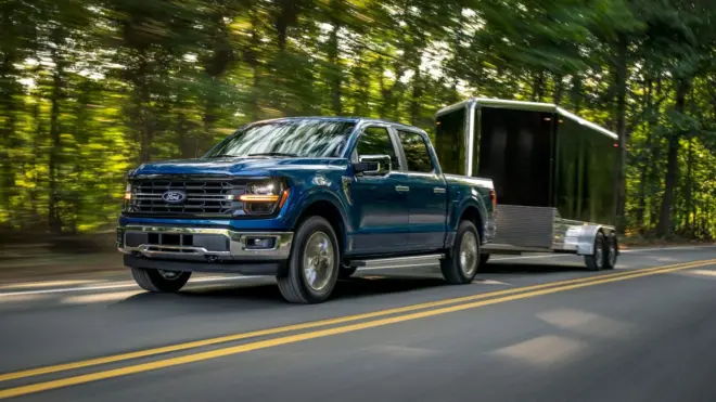 Blauer Ford F-150 EcoBoost fährt mit einem schwarzen Kastenanhänger auf einer Landstraße