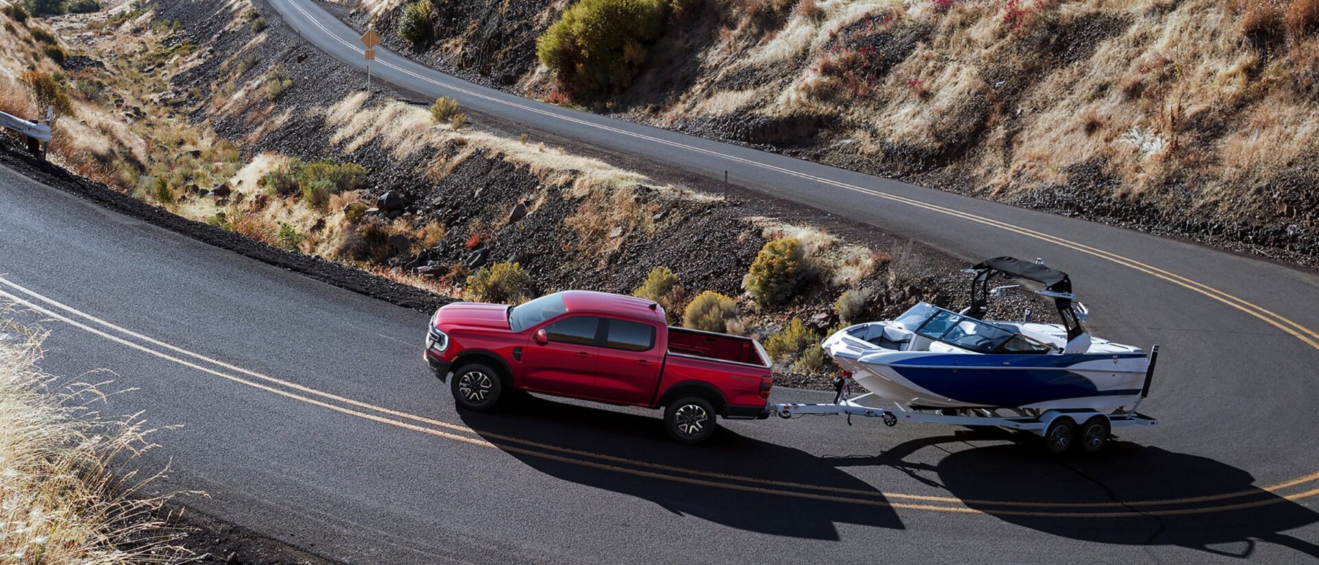 Roter Ford Ranger zieht ein Motorboot auf einem Doppelachsanhänger über eine Bergstraße