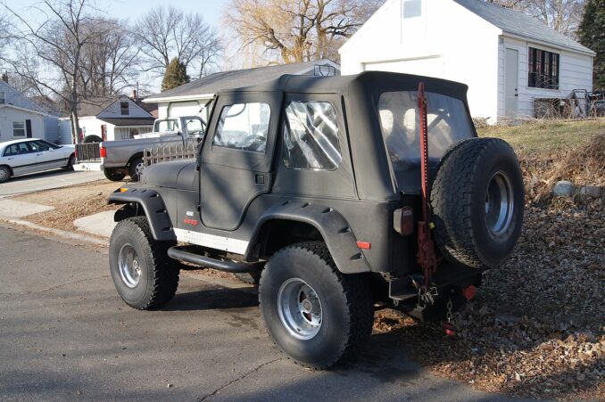 Schwarzer Jeep CJ-5 von 1976 mit großen Geländereifen Reserverad und Hi-Lift-Wagenheber