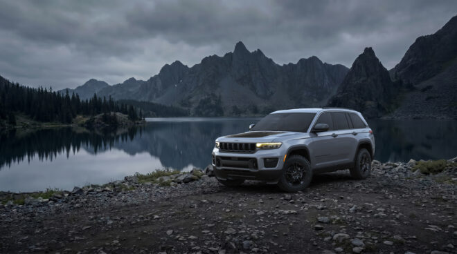 Silbergrauer Jeep Grand Cherokee Laredo Upland 2027 in Front-Dreiviertelansicht an einem Bergsee