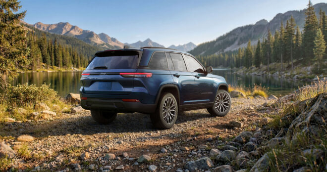 Blauer Jeep Grand Cherokee Overland 2027 in Heck-Dreiviertelansicht vor einem Bergsee