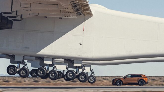 Porsche Cayenne Turbo Electric fährt neben dem riesigen Hauptfahrwerk des Stratolaunch Roc