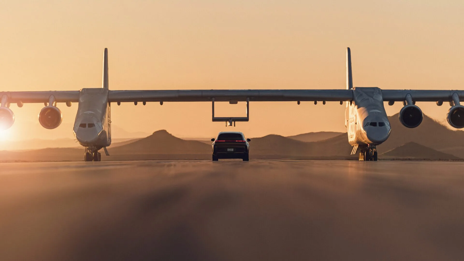 Porsche Cayenne Turbo Electric unter dem Stratolaunch Roc beim Sonnenuntergang