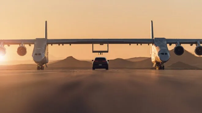Porsche Cayenne Turbo Electric unter dem Stratolaunch Roc beim Sonnenuntergang