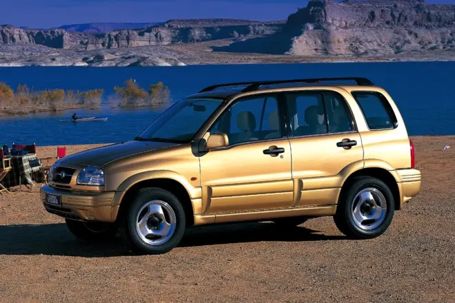 Goldener Suzuki Grand Vitara der ersten Generation in Front-Dreiviertelansicht an einem See